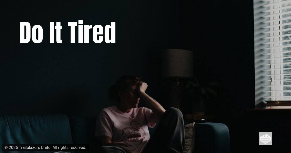 A person sits on a couch in a dimly lit room, head resting on their hand, with light coming through a nearby window.