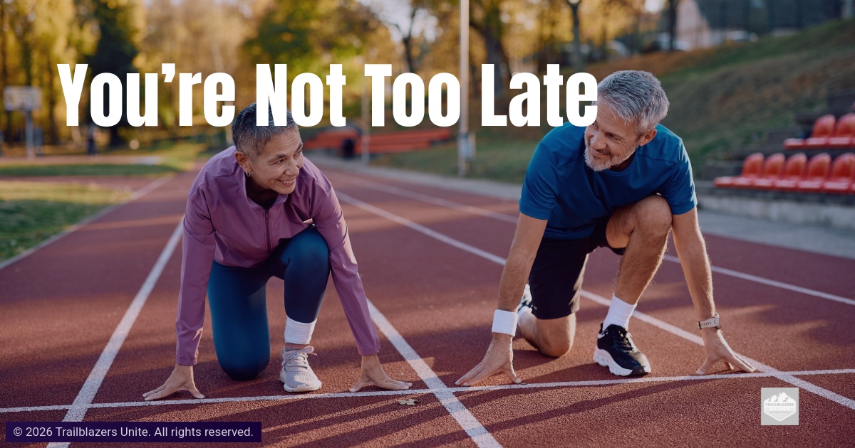 Two older adults crouch at a running track starting line, smiling and preparing to move forward.
